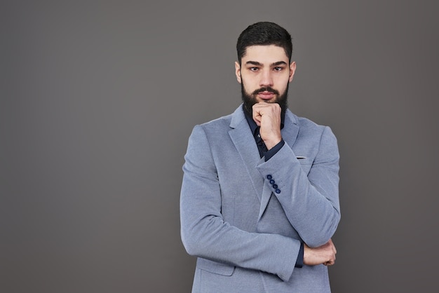 Retrato de freelancer homem com barba em pé de jaqueta contra o pano de fundo cinza.