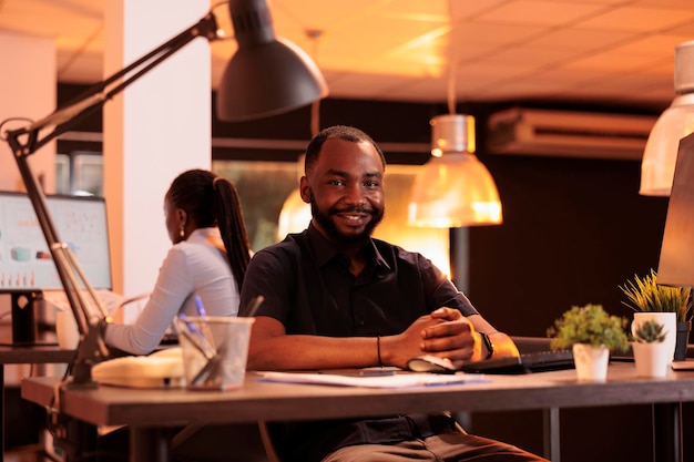 Retrato de funcionário da empresa trabalhando no computador na mesa durante o pôr do sol, usando rede de dados. Criação de apresentação de negócios com pesquisa e informações para fazer relatório em escritório com grandes janelas.