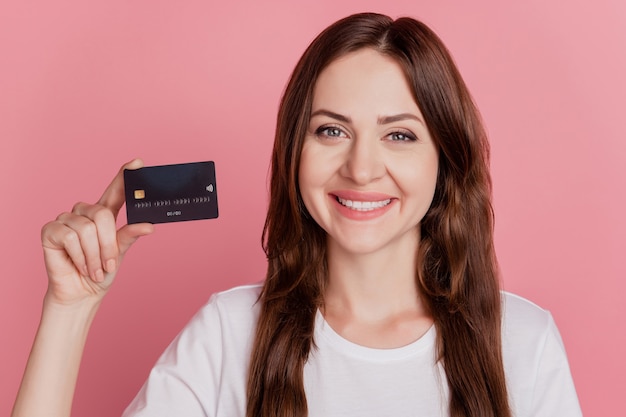 Retrato de garota promotora positiva demonstra sorriso brilhante de cartão de crédito em fundo rosa