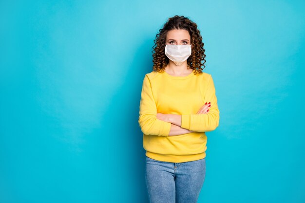 Retrato de garota séria usando máscara médica segura sars ncov-2 de braços cruzados fundo azul