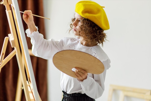 Retrato de garotinha artista de boina amarela que pinta imagens em estúdio enquanto segura palete