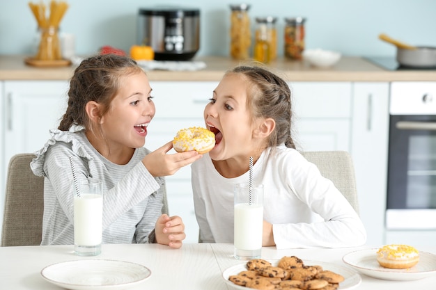 Retrato de gêmeas fofas comendo donuts com leite na cozinha