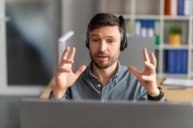 Retrato de gerente masculino concentrado no fone de ouvido com chamada web no pc sentado na mesa no local de trabalho