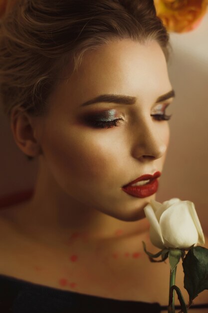 Foto retrato de glamour de uma mulher loira elegante de olhos fechados segurando uma rosa branca perto do rosto