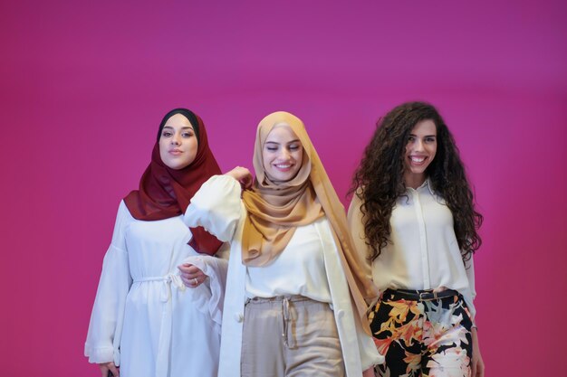 retrato de grupo de belas mulheres muçulmanas, duas delas em vestidos elegantes com hijab isolado em fundo rosa, representando a moda islâmica moderna e o conceito de ramadan kareem