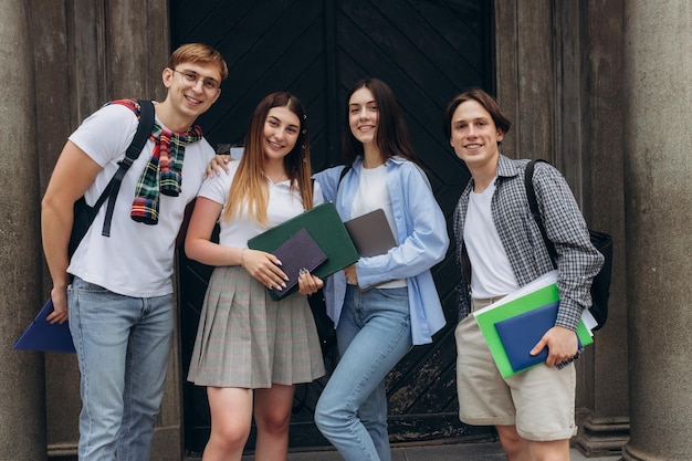 Retrato de grupo de estudantes sorridentes com livros e mochilas olhando para o conceito de educação da câmera