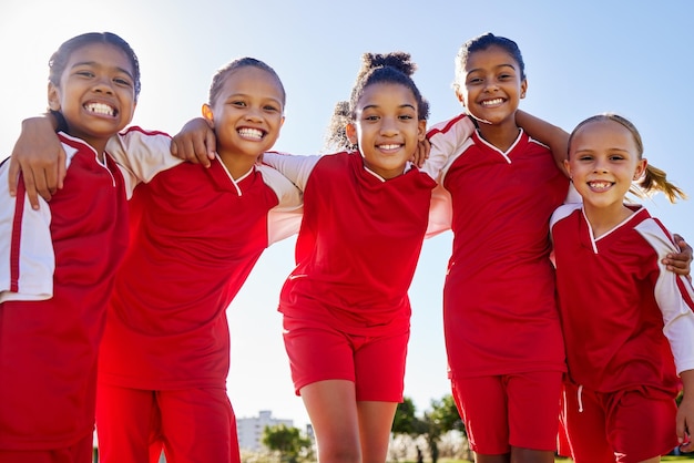 Retrato de grupo de garotas de futebol e campo para sorriso construção de equipes felicidade e solidariedade no treinamento esportivo Diversidade esportiva de crianças do sexo feminino e amigos com aprendizado de trabalho em equipe ou futebol com ângulo baixo