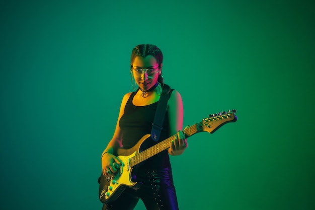 Foto retrato de guitarrista feminino isolado na parede verde do estúdio com luz de néon