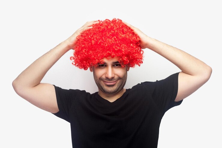 Foto retrato de hipster louco, homem alegre com cerdas e camiseta tocando peruca vermelha na cabeça e sorrindo para a câmera, parecendo engraçado com cabelo brilhante. tiro de estúdio interior isolado no fundo branco