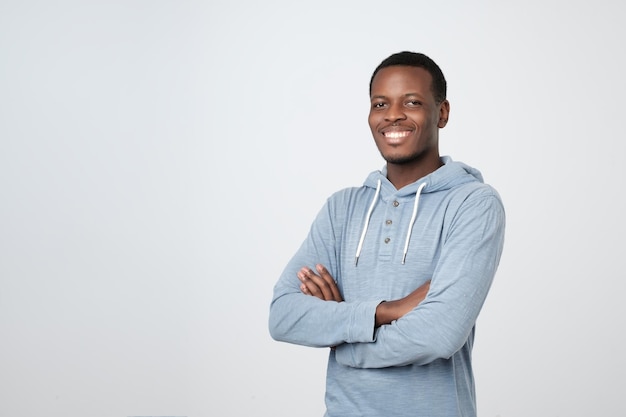 Retrato de homem africano bonito feliz na camisa azul cruzando as mãos e olhando para a câmera