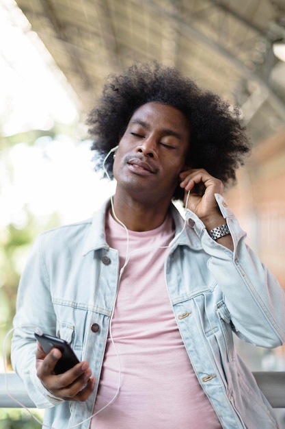 Retrato de homem afro-americano com roupas casuais e penteado afro curtindo música de seu telefone inteligente Momentos engraçados e relaxantes