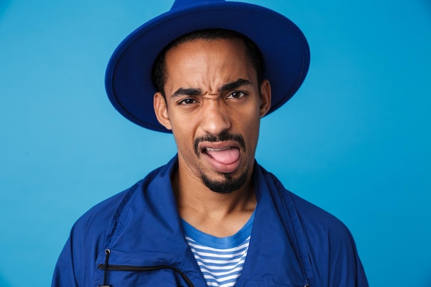 Retrato de homem afro-americano descontente com chapéu fazendo careta isolada no azul