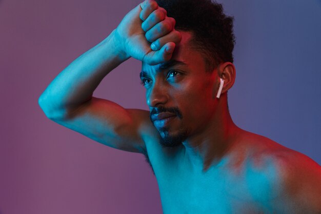 Retrato de homem afro-americano sem barbear, posando com um fone de ouvido isolado sobre a parede violeta