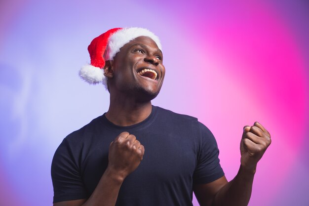 Retrato de homem afro-americano sorridente positivo com chapéu de Papai Noel e camiseta casual em colorido