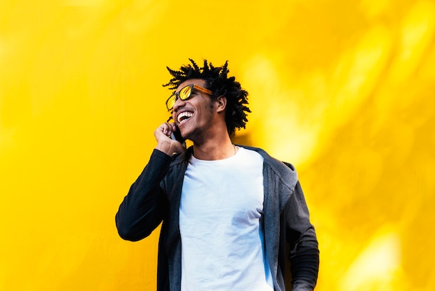 Retrato de homem afro bonito usando seu celular na rua.