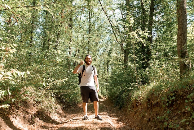 Retrato de homem alegre alpinista barbudo com mochila aparecendo o polegar.