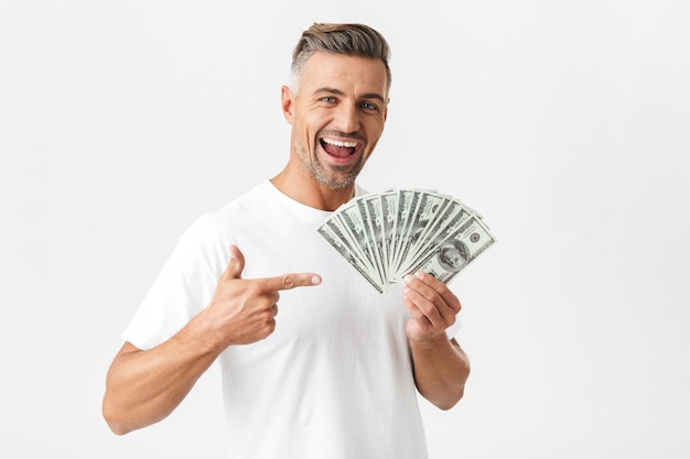 Retrato de homem alegre dos anos 30, vestindo camiseta casual, sorrindo e segurando um monte de notas de dinheiro isoladas em branco