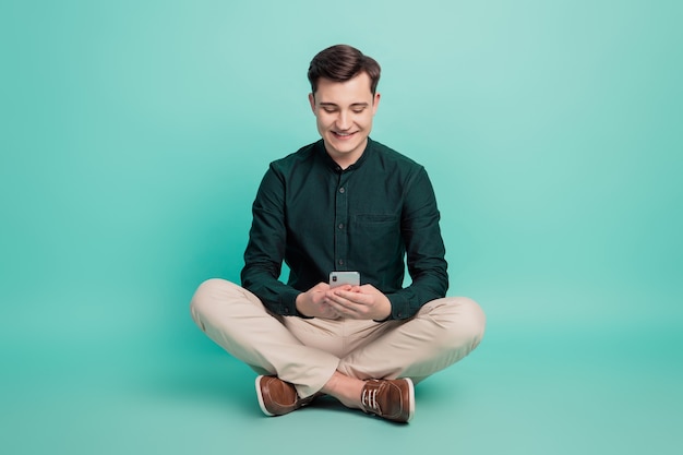 Retrato de homem alegre segurando telefone, tela, compartilhar postagens nas redes sociais no fundo azul-petróleo