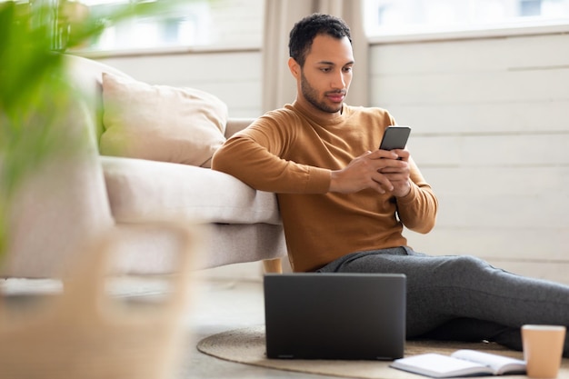 Retrato de homem árabe usando smartphone e pc em casa