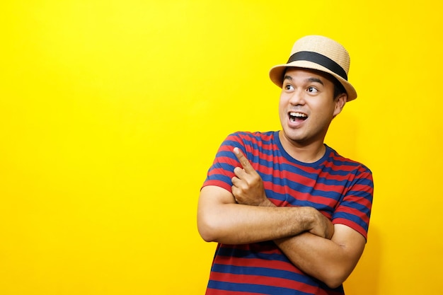 Retrato de homem asiático alegre em roupas básicas casual usar camiseta listrada vermelha e usar um chapéu sorrindo e mostrar dando polegares para a câmera com mostrando sucesso isolado sobre fundo amarelo