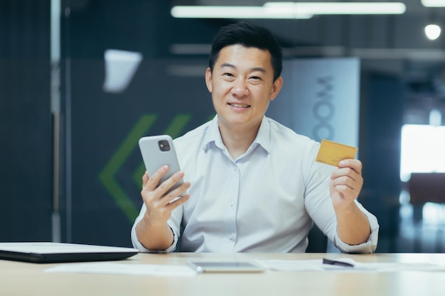 Retrato de homem asiático bem sucedido no empresário de escritório olhando para a câmera e sorrindo segurando o banco