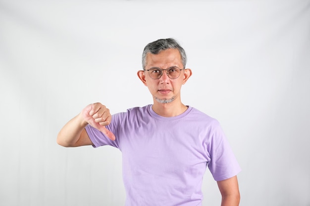 Retrato de homem asiático vestindo camiseta casual parecendo infeliz mostrando rejeição com os polegares para baixo