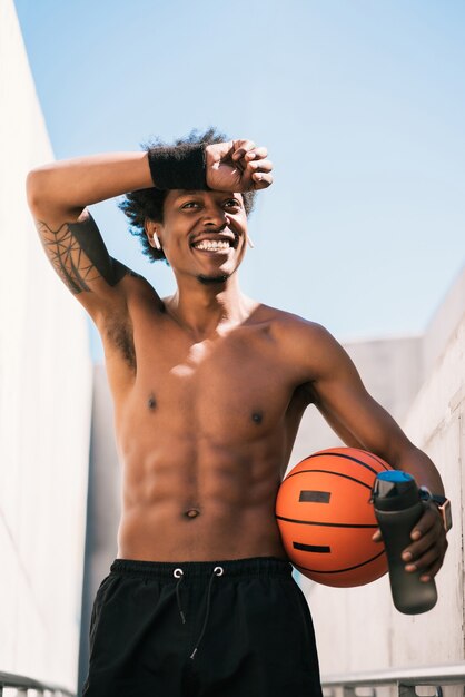 Retrato de homem atleta afro, segurando uma bola de basquete e relaxante após o treino ao ar livre. esporte e estilo de vida saudável.