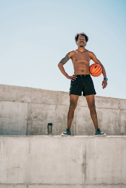 Retrato de homem atleta afro segurando uma bola de basquete em pé ao ar livre. esporte e estilo de vida saudável.