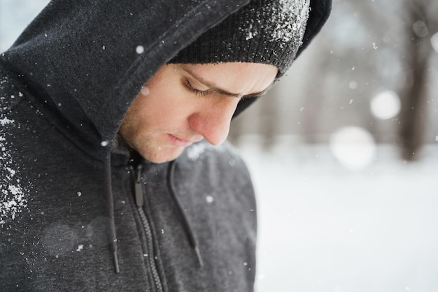 Retrato de homem atlético bonito vestindo capuz durante seu treino de inverno no parque da cidade de neve