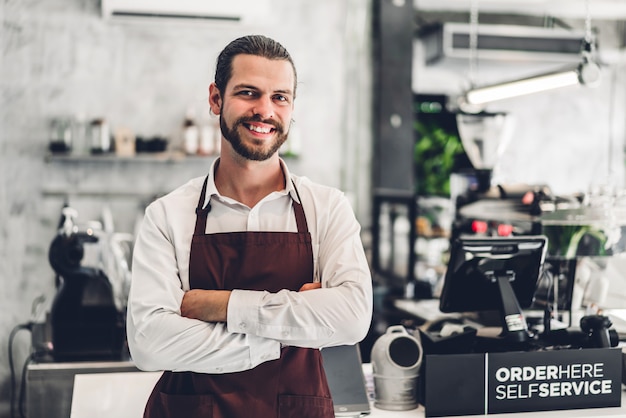 Retrato de homem barbudo bonito barista empresário pequeno empresário sorrindo atrás da barra de balcão em um café