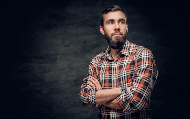 Retrato de homem barbudo com braços cruzados, vestido com uma camisa xadrez vermelha.