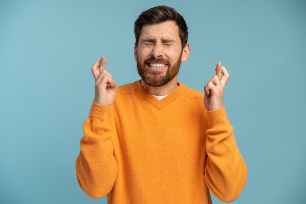 Retrato de homem barbudo cruzando os dedos e fechando os olhos fazendo desejo acreditando na esperança milagrosa no sucesso tiro de estúdio interior isolado em fundo azul