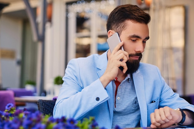 Retrato de homem barbudo elegante em uma jaqueta azul fala pelo smartphone.