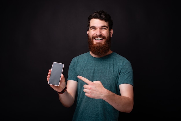 Retrato de homem barbudo espantado, apontando para o seu smartphone