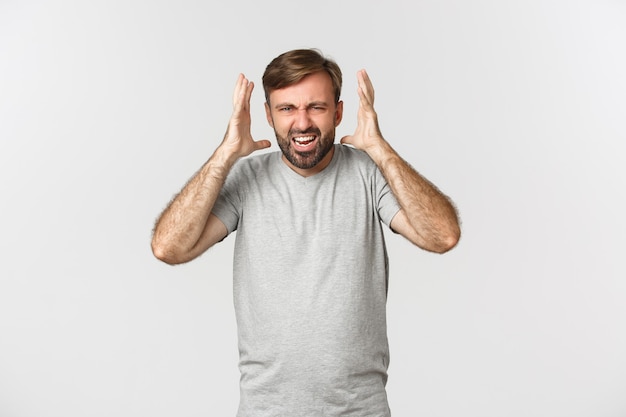 Retrato de homem barbudo furioso, gritando e apertando as mãos frustrado, furioso com o branco