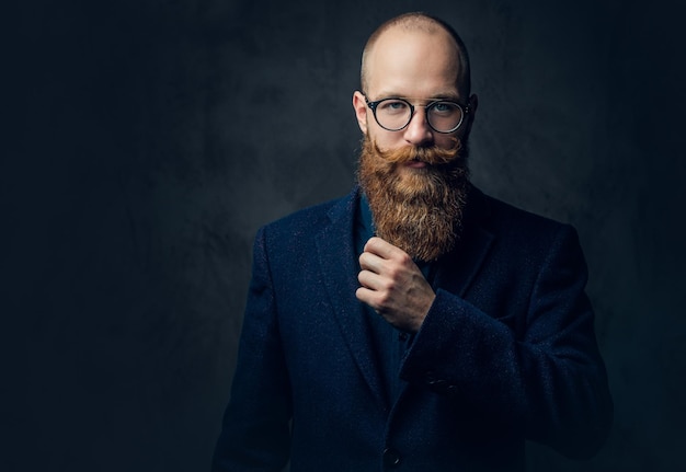 Retrato de homem barbudo ruiva em óculos vestido com um terno de lã elegante sobre fundo cinza.