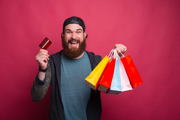 Retrato de homem barbudo sorridente feliz segurando sacolas e cartão de crédito