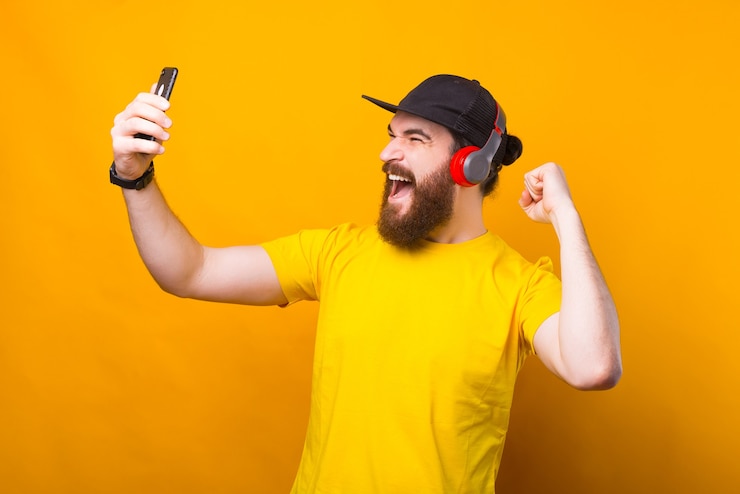 Foto retrato de homem barbudo surpreso usando smartphone e ouvindo música em fones de ouvido