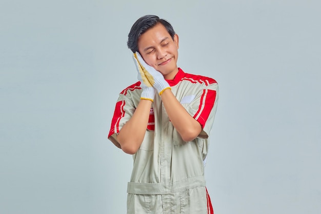 Retrato de homem bonito alegre vestindo uniforme mecânico com gesto para dormir em fundo cinza