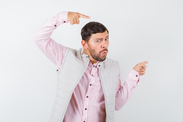 Retrato de homem bonito apontando para o lado direito em colete, camisa e parecendo surpreso