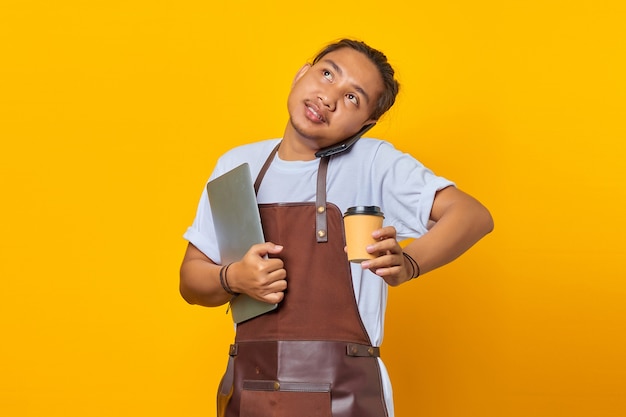 Retrato de homem bonito asiático ocupado atendendo chamadas. ambas as mãos carregando um laptop e uma xícara de café