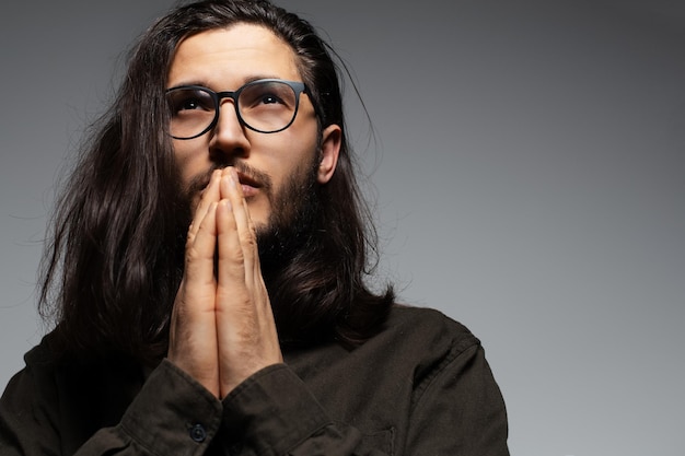 Retrato de homem bonito com cabelo comprido, de mãos dadas em gesto de oração