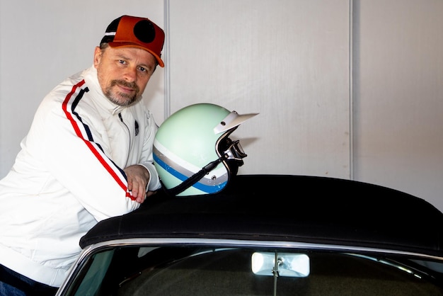 Retrato de homem bonito de homem caucasiano de meia idade corrida de carro jaqueta branca vintage e capacete de corrida retrô