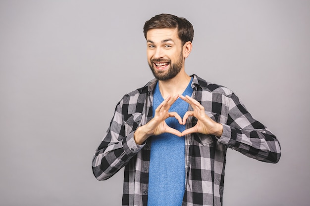 Retrato de homem bonito feliz em casual fazendo sinal de coração com os dedos.