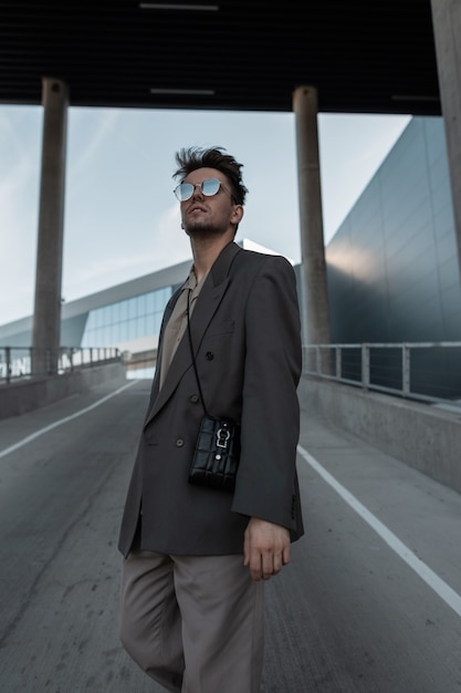 Retrato de homem bonito na moda cinza com óculos de sol no meio urbano