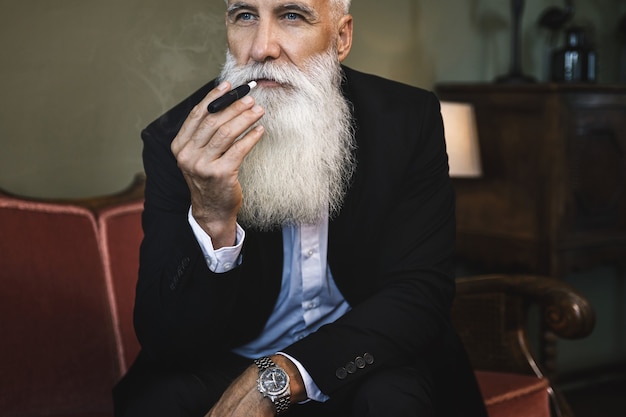 Retrato de homem bonito sênior fumando sistema de aquecimento de tabaco