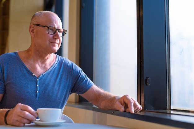 Retrato de homem bonito turista escandinavo sênior relaxando dentro de uma cafeteria