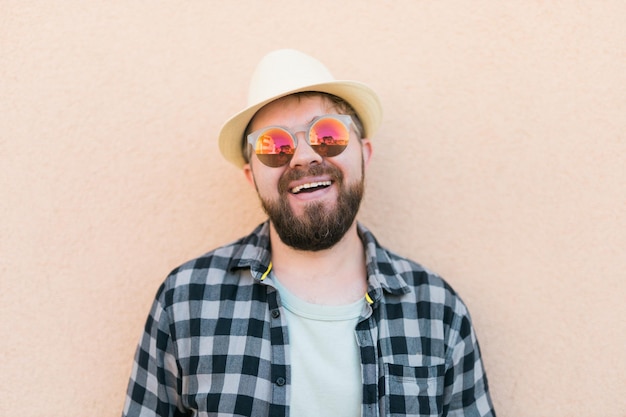 Retrato de homem bonito usando chapéu de verão e camisa xadrez sorrindo feliz perto de férias de viagem de parede e conceito de férias de verão