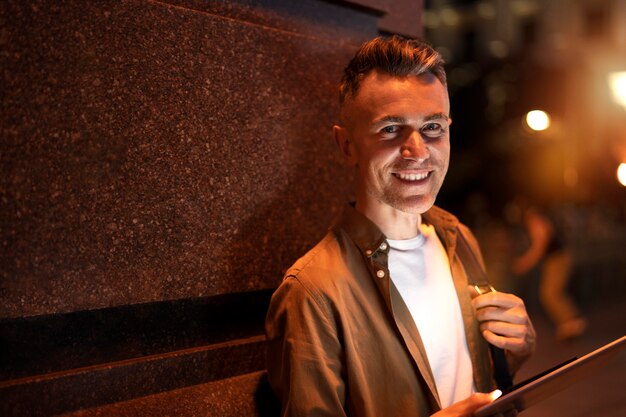 Foto retrato de homem bonito usando tablet à noite nas luzes da cidade