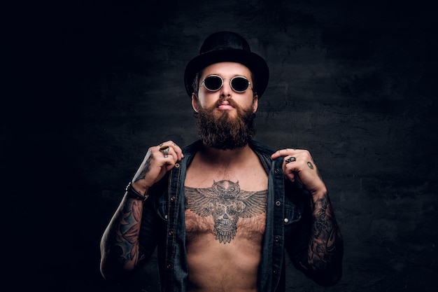 Retrato de homem brutal com camisa jeans aberta e peito tatuado.
